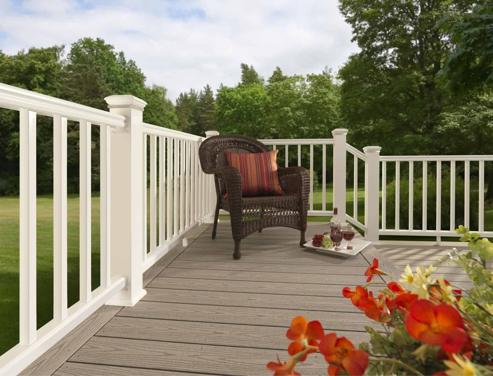 Wicker chair with cushions placed on a wooden deck surrounded by flowers and greenery.