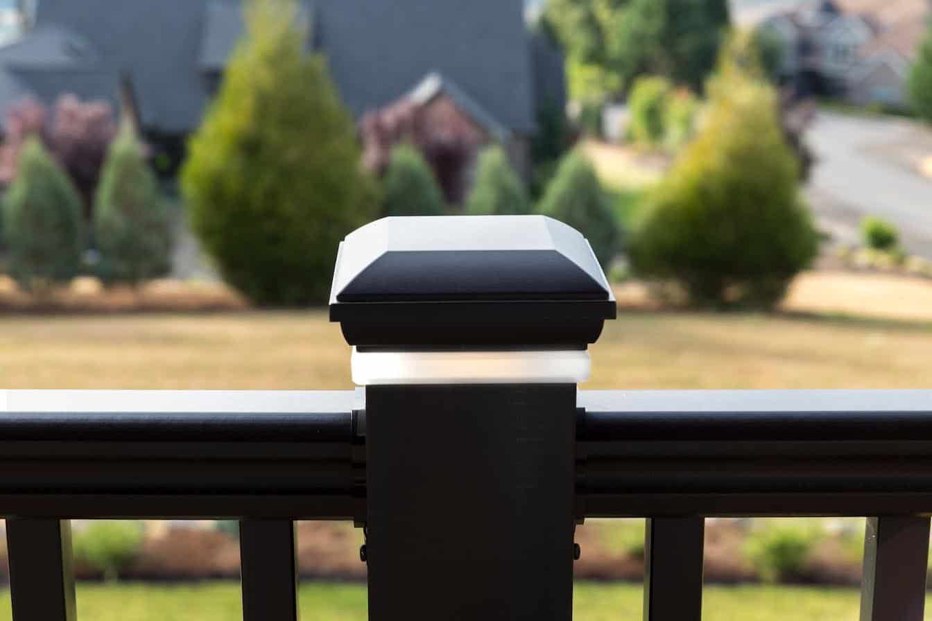 Black composite railing post with a decorative cap in focus, overlooking a blurred landscape.