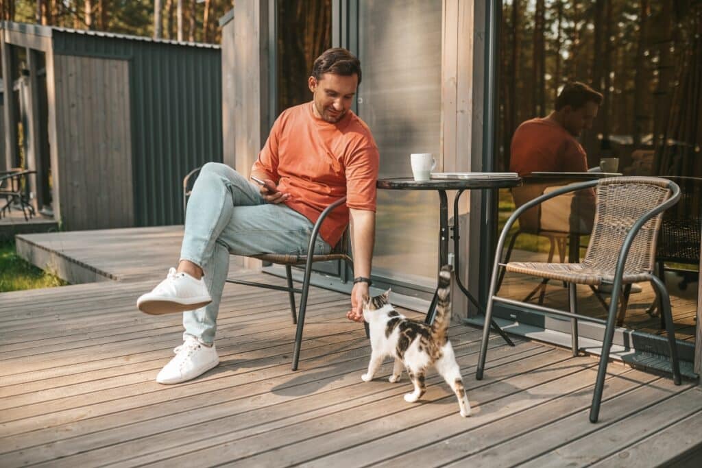 A man petting a cat and enjoying the composite decking benefits.